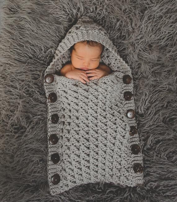 a baby wrapped up in a crochet blanket on top of a furry rug