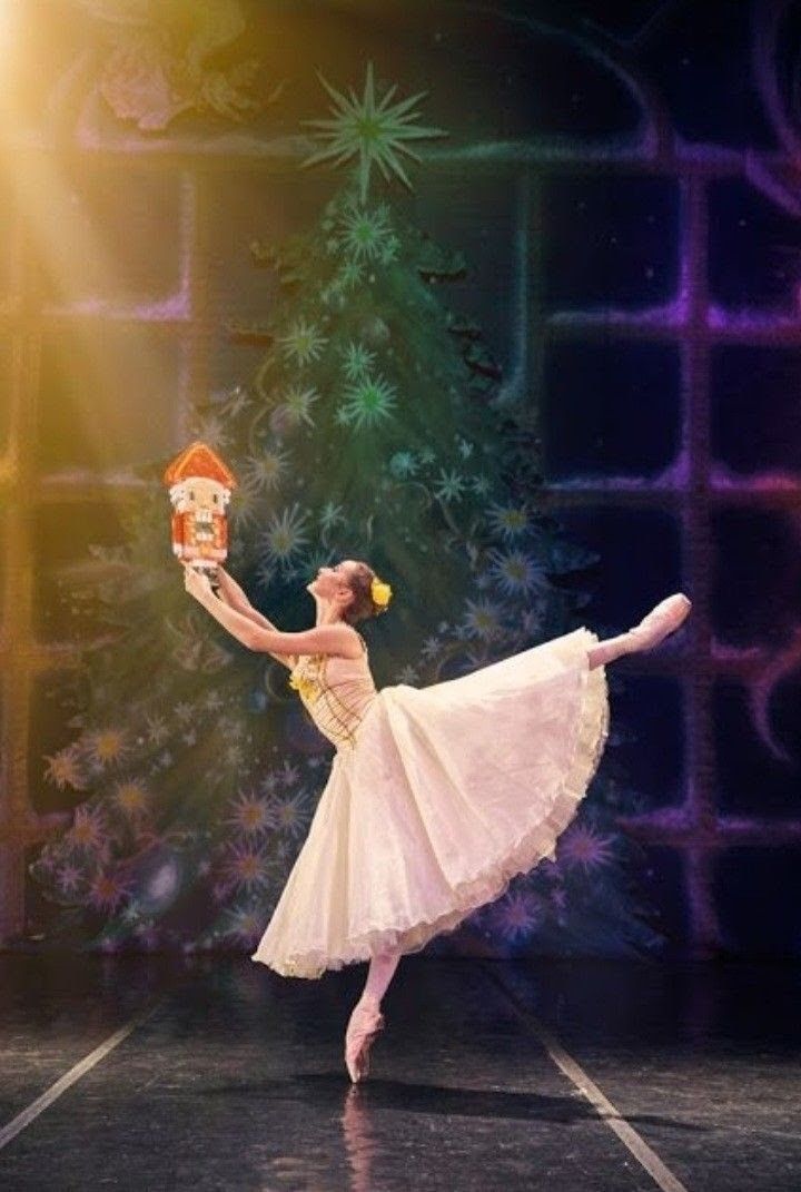 a ballerina in a white dress is performing on stage with a christmas tree behind her