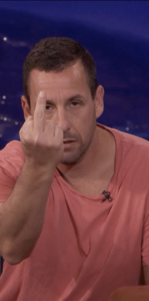 a man in a pink shirt pointing at the camera with his finger to his face