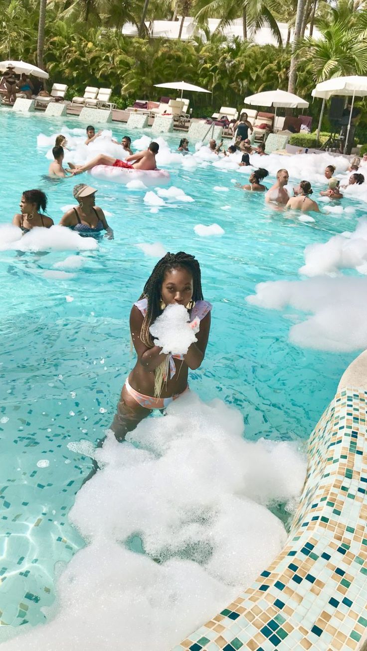 a woman standing in the middle of a swimming pool surrounded by clouds and umbrellas