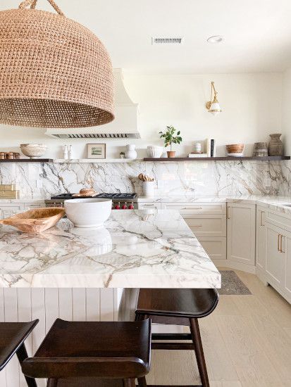 a white kitchen with marble counter tops and wooden stools in front of the sink