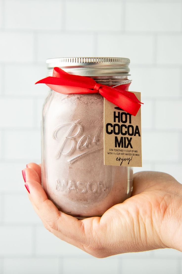 a hand holding a mason jar with hot cocoa mix in it and a red ribbon around the top