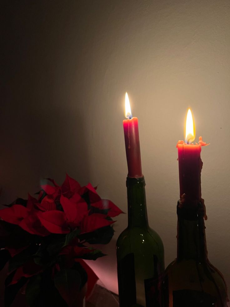 two wine bottles with candles in them sitting next to a vase filled with red flowers