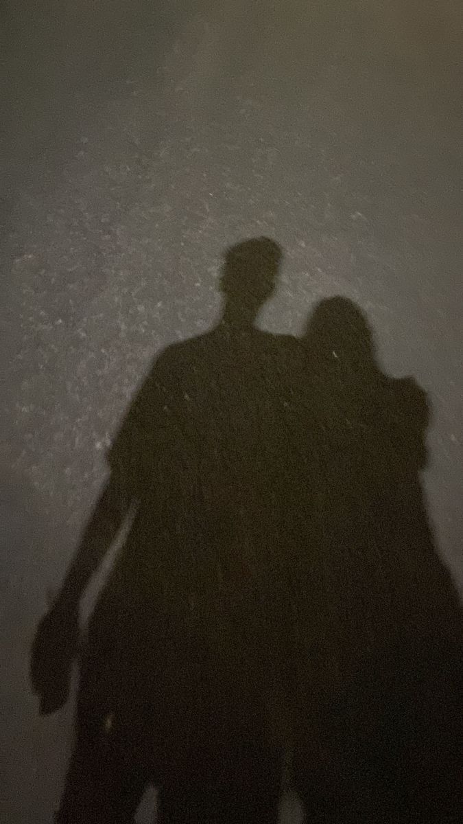 two people standing next to each other in the dark with their shadows on the ground