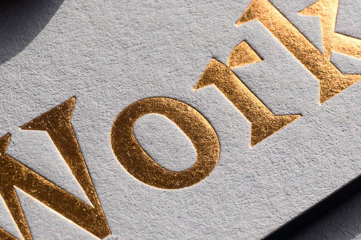 the word now is written in gold on a white surface with metallic letters and arrows