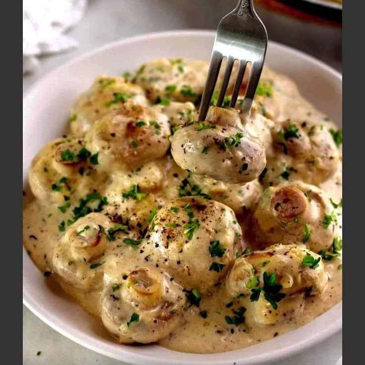 a white plate topped with dumplings covered in gravy next to a fork