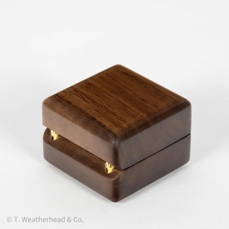 a wooden box with two gold studs on the inside and outside, sitting on a white surface