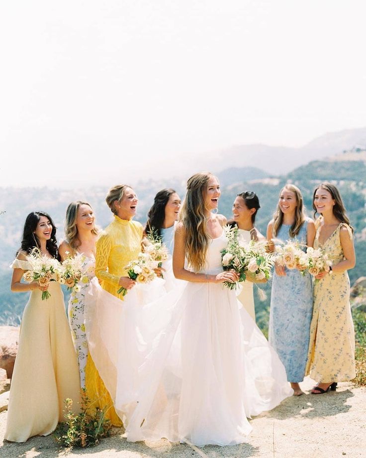 a group of women standing next to each other on top of a hill holding bouquets