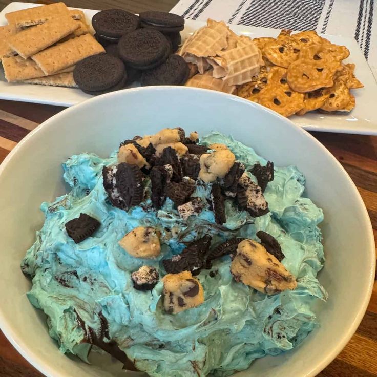 a bowl filled with ice cream and cookies on top of a table next to plates of crackers