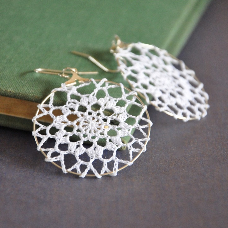 the earrings are made with white crochet and gold plated wire, on top of a green book