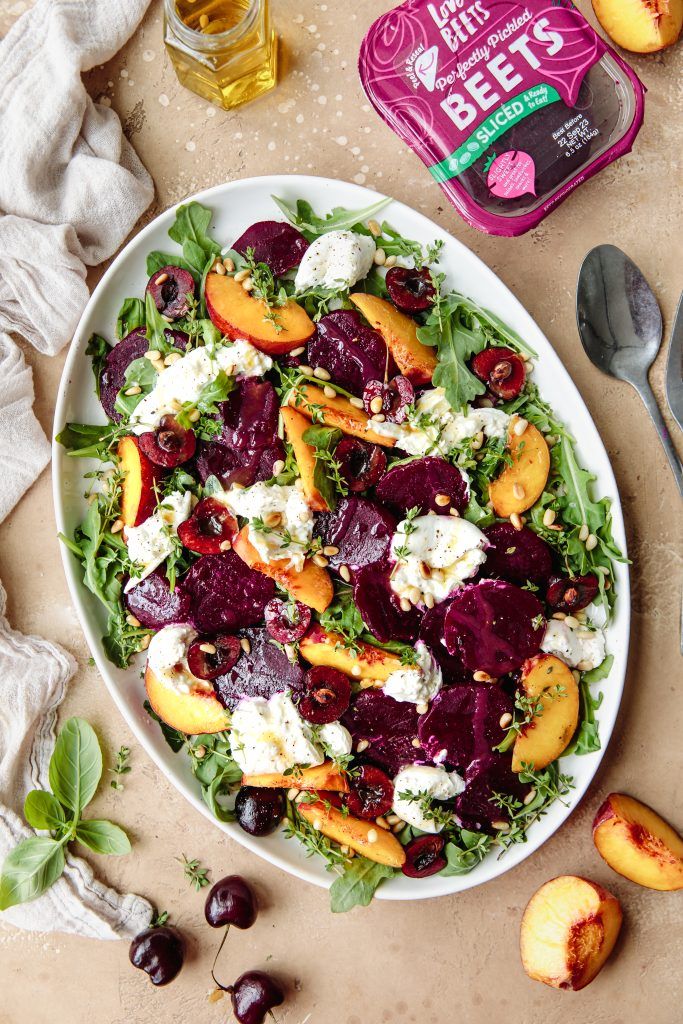 a salad with beets, goat cheese and cherries in a white bowl on a table