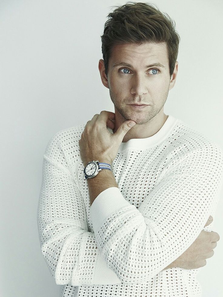 a man with his hand on his chin looking at the camera while wearing a white sweater