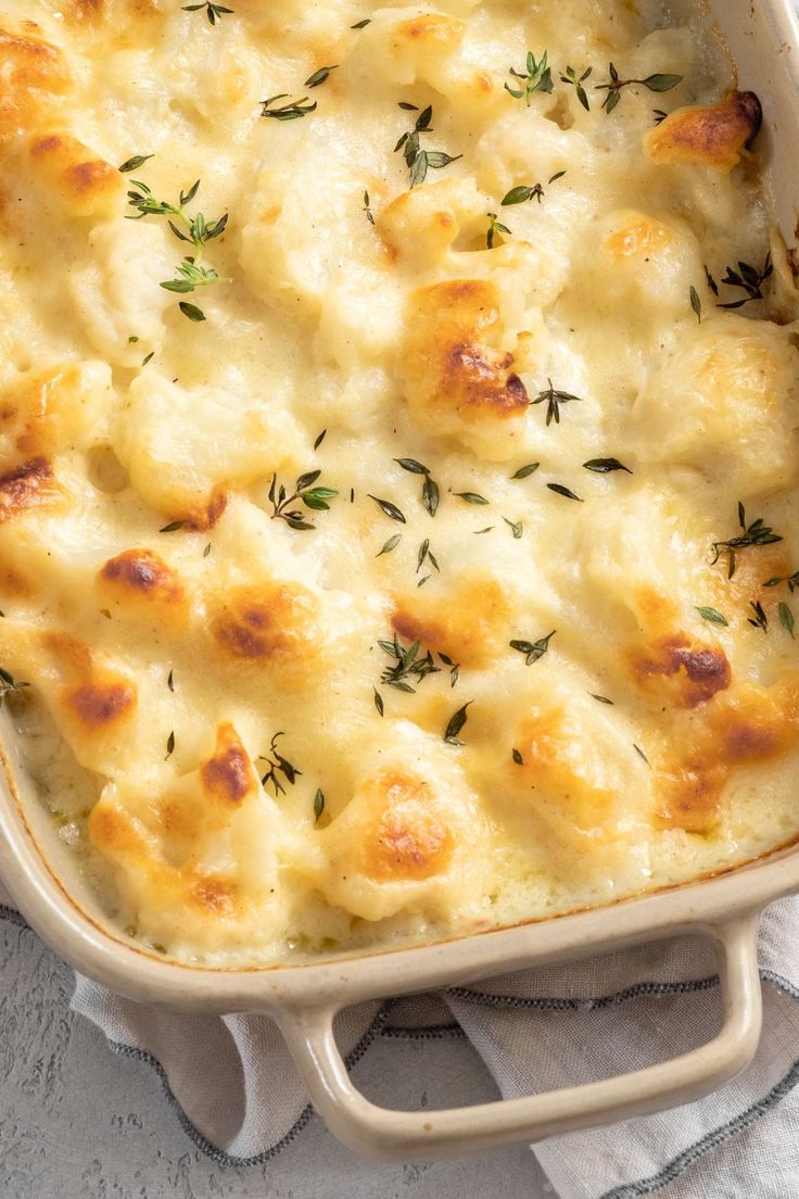 a casserole dish with cheese and herbs in it sitting on a white towel