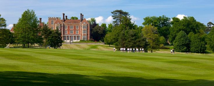 people are playing golf in front of a large building with trees on the other side