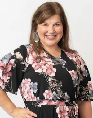 a woman in a floral dress smiling at the camera with her hands on her hips