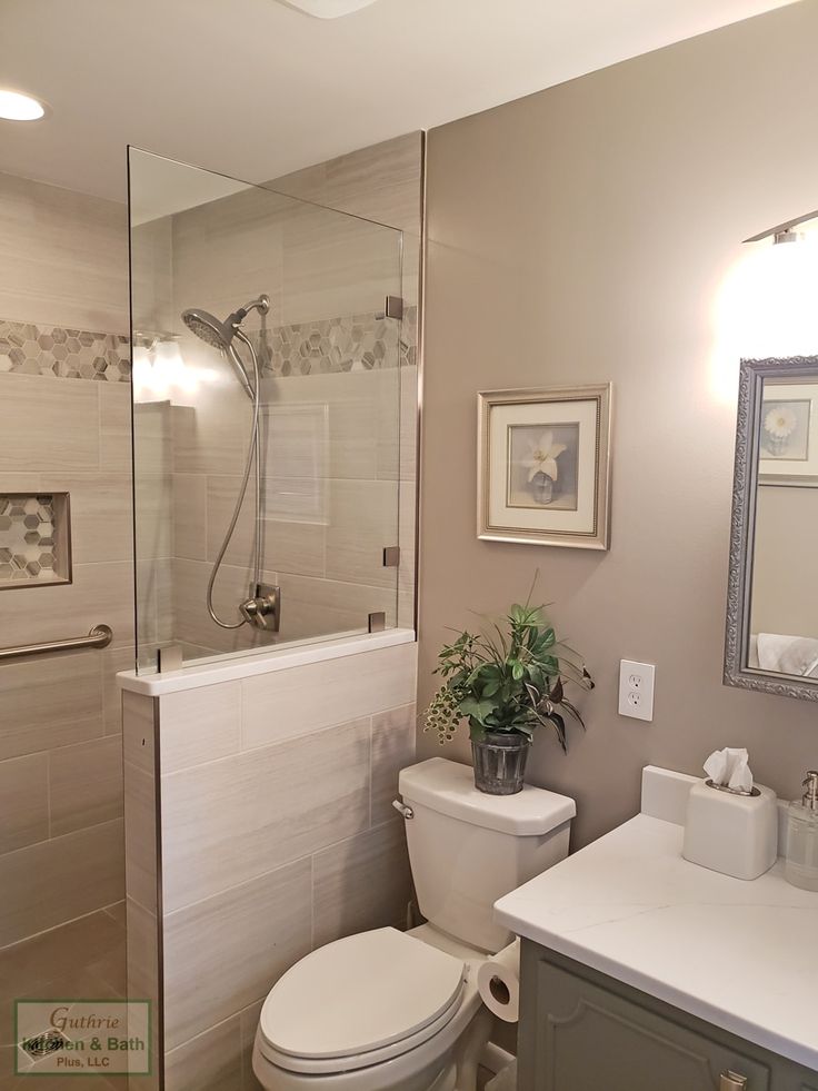 a white toilet sitting next to a walk in shower under a bathroom mirror above a sink