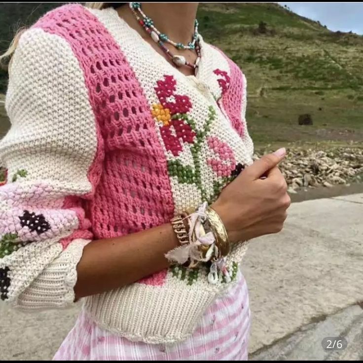 a woman wearing a pink and white knitted sweater with flowers on the sleeves is holding her cell phone