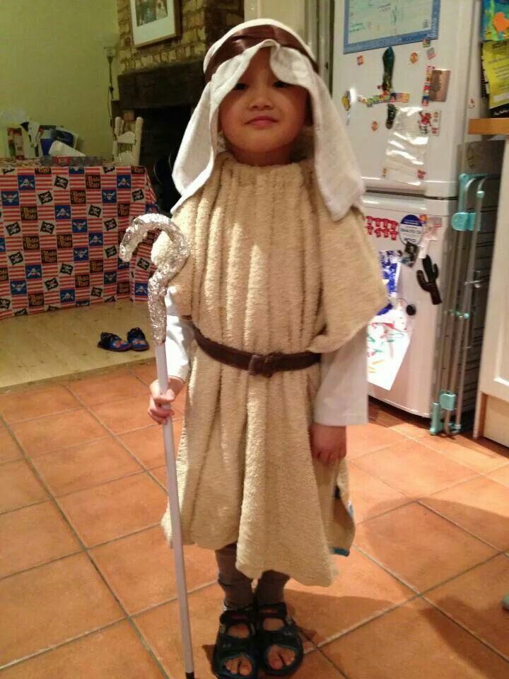 a little boy dressed up like jesus with a stick in his hand, standing on the kitchen floor