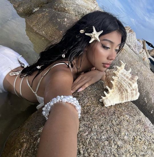 a beautiful woman laying on top of a rock next to the ocean holding a starfish