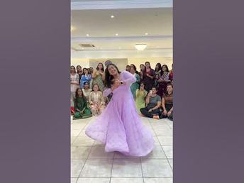 a woman in a purple dress is dancing on the dance floor with people behind her