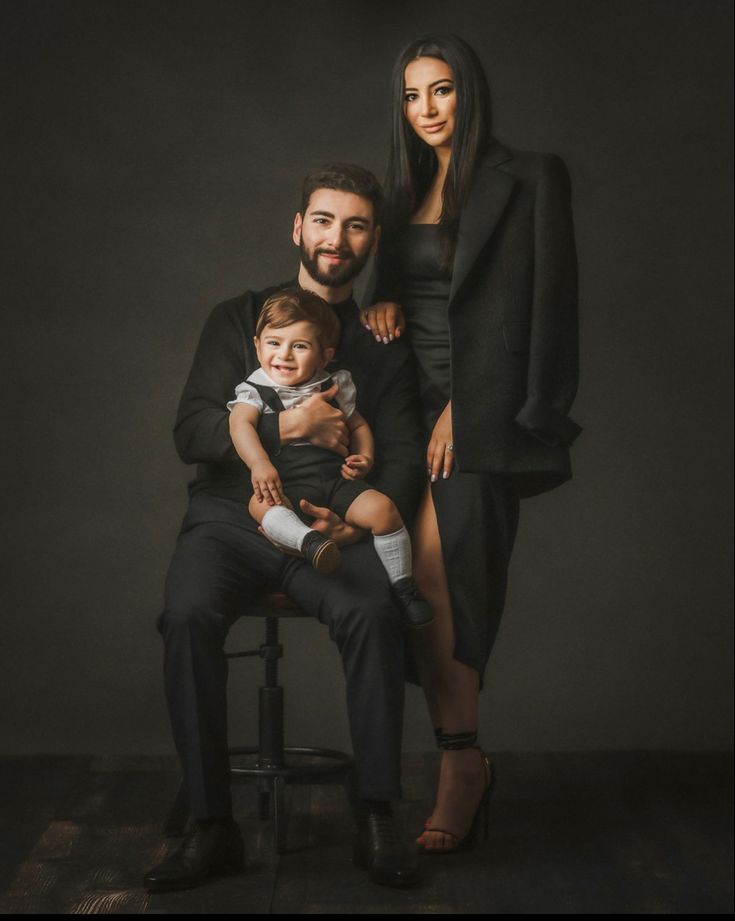 a man, woman and child are posing for a photo in front of a dark background