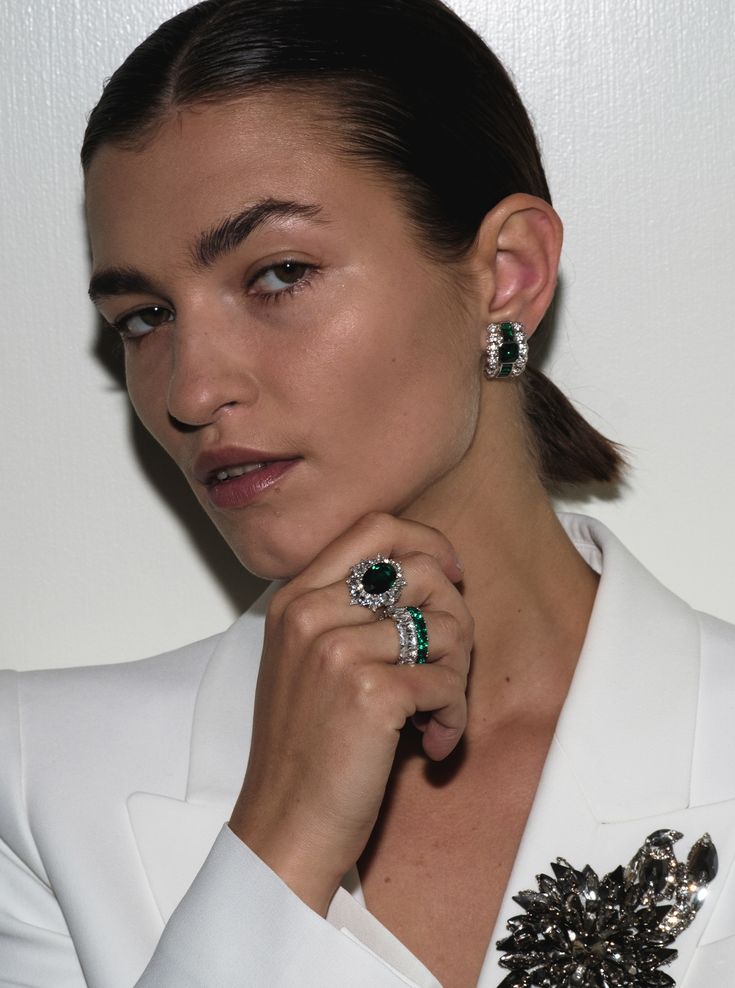 a woman in a white blazer and matching earrings poses for the camera with her hand on her shoulder