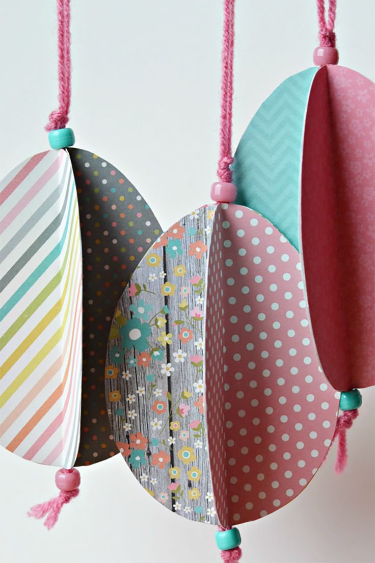 three colorful paper easter eggs hanging from strings on a white wall with polka dotes