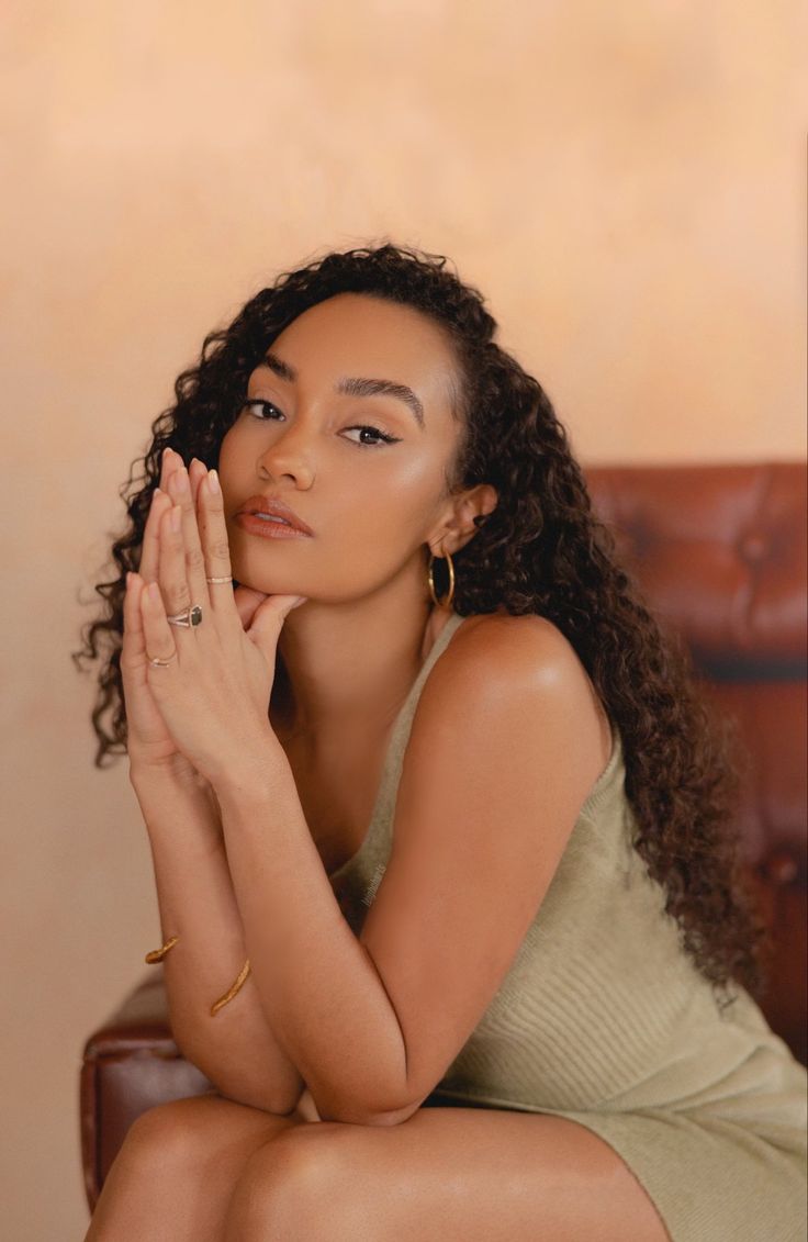 a woman sitting on top of a brown couch with her hands clasped in front of her face