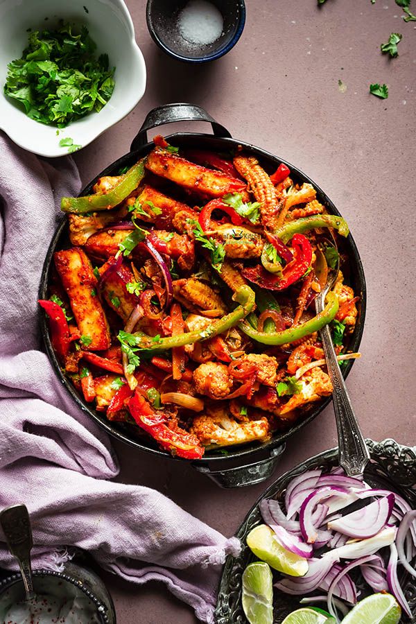 a skillet filled with chicken, peppers and onions next to sliced lime wedges