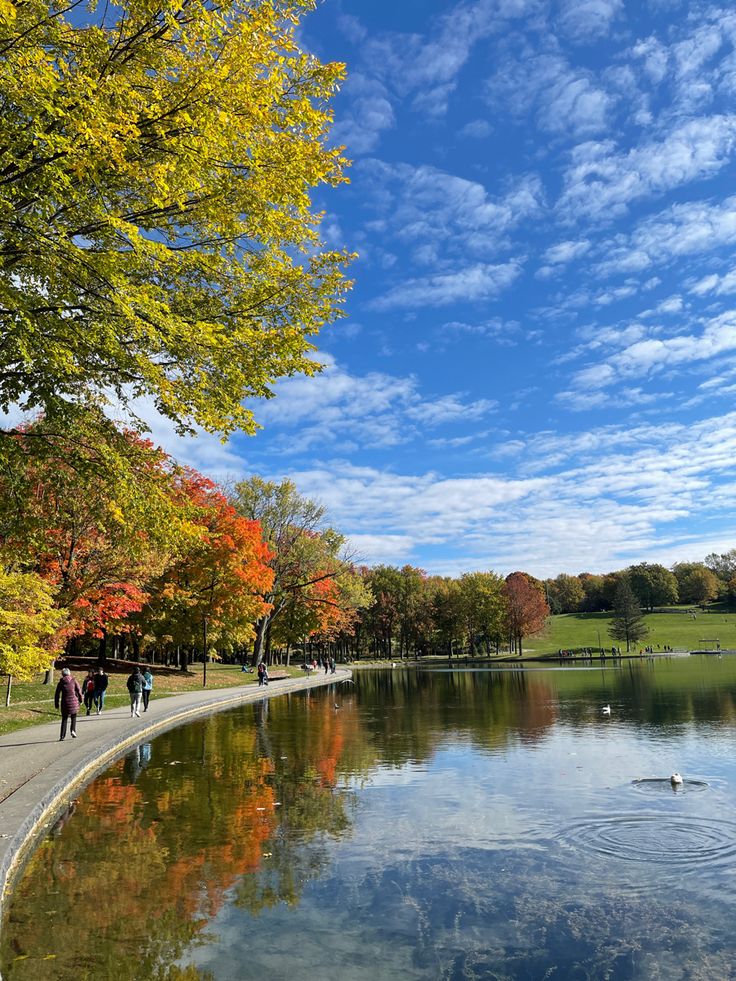 people are walking along the edge of a lake in autumn with colorful trees surrounding it