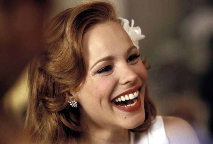 a smiling woman wearing a white dress and flower in her hair, holding a cell phone to her ear