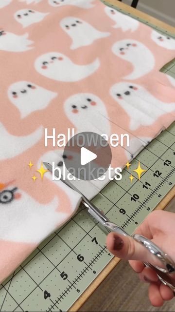 someone using scissors to cut fabric with halloween ghost on pink and white background, while another person is cutting the fabric