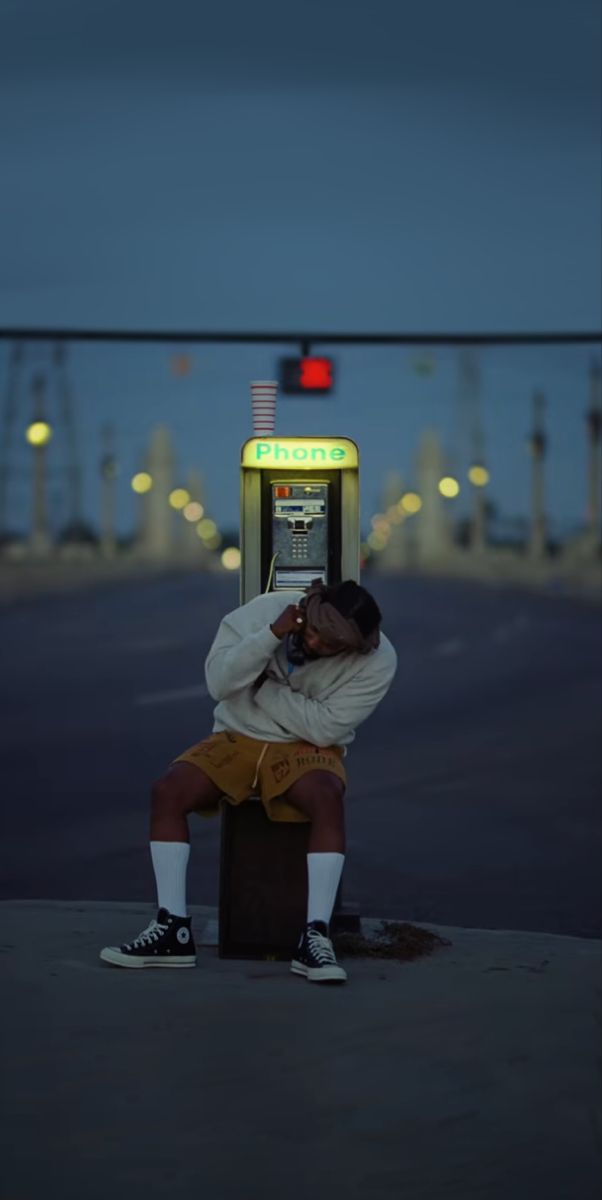 a man sitting on top of a box talking on a cell phone next to a street