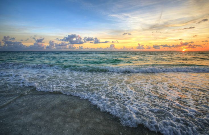 the sun is setting over the ocean with waves crashing on the shore and clouds in the sky