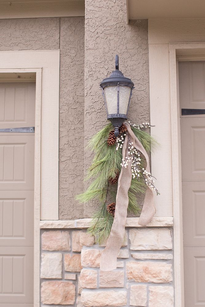 a street light hanging from the side of a building next to a wreath and pine cones