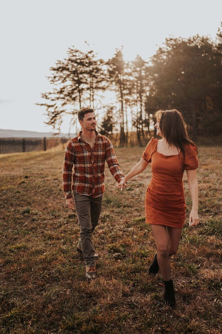 a man and woman holding hands walking through an open field