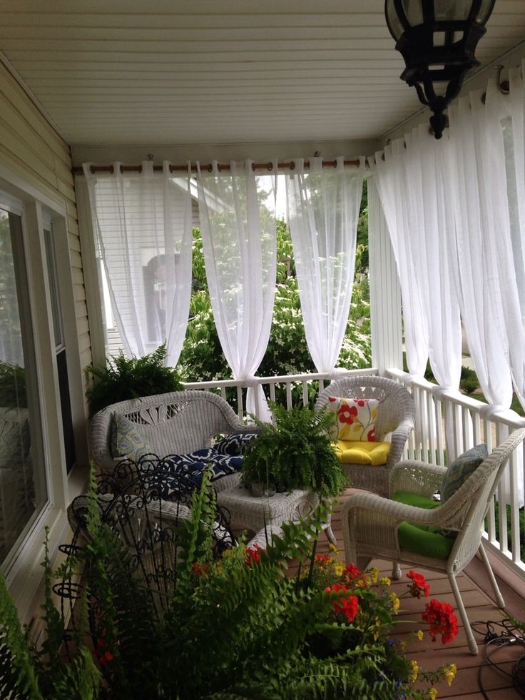 the porch is covered with white curtains and wicker furniture, along with potted plants