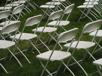 rows of white folding chairs sitting in the grass