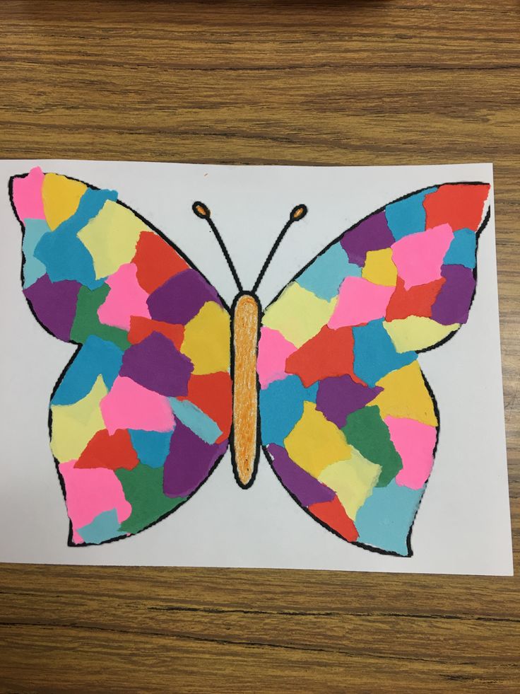 a butterfly made out of colored paper on top of a wooden table next to a pencil