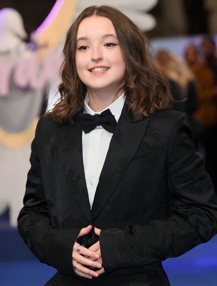 a woman in a tuxedo and bow tie smiles at the camera while standing