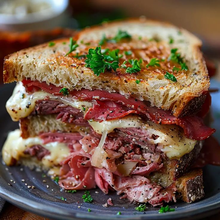 a roast beef sandwich with melted cheese and herbs on a plate, ready to be eaten