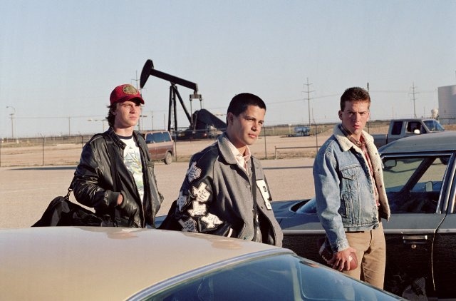 three men standing next to each other in front of a car with an oil pump behind them