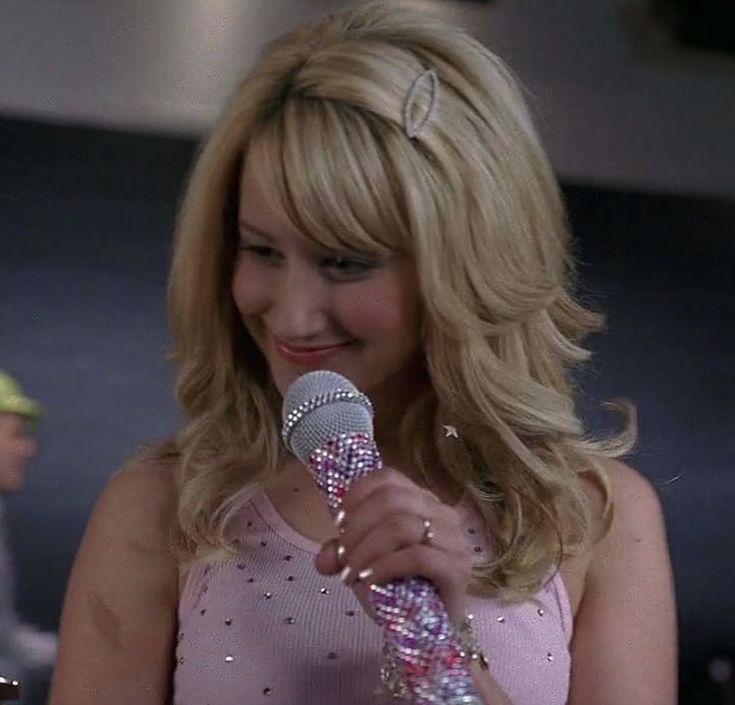 a woman holding a microphone in her right hand and wearing a pink dress with sequins on it