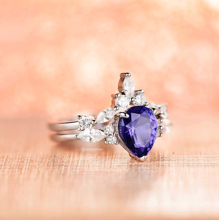 Gorgeous Vintage Inspired Tanzanite Ring Set►Made of 925 solid sterling silver with rhodium finish ►Accented with simulated diamonds (CZ)►Average band width: 1.7 mm►Sold as a setCenter Stone: Tanzanite Shape: Teardrop/ PearGem size: 7 x 9 mmCarat Weight: 1.7 ct. (approx.)Gemstone Creation: Simulated Hardness: 8 (Mohs scale)✓ 100% Nickel-Free✓ Hypoallergenic✓ Comfort Fit✓ Free Ring Box✓ Free USA Shipping Trillion Cut Tanzanite White Gold Jewelry, Trillion Cut Tanzanite Jewelry In White Gold, Heart Cut Tanzanite Jewelry For Anniversary, Dazzling Tanzanite Diamond Wedding Ring, Dazzling Brilliant Cut Sapphire Ring In Sterling Silver, White Gold Tanzanite Rings With Vvs Clarity, Trillion Cut Tanzanite Rings For Wedding, White Gold Tanzanite Birthstone Ring For Wedding, Dazzling Sterling Silver Sapphire Ring