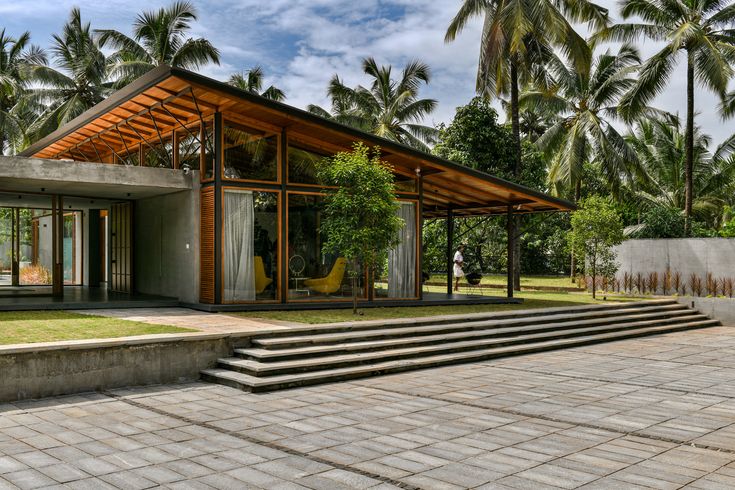 a modern house with steps leading up to the front door and covered patio, surrounded by palm trees