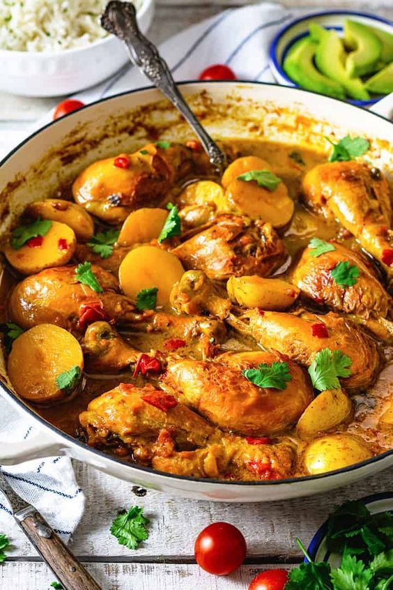 chicken and potatoes stew in a pan with tomatoes, parsley and rice on the side