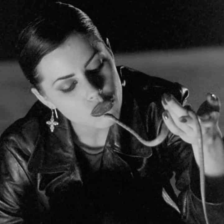 a woman in black leather jacket blowing on a pipe with her mouth open and tongue out