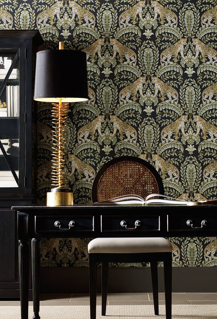 a desk with a lamp, chair and book on it in front of a wallpapered background