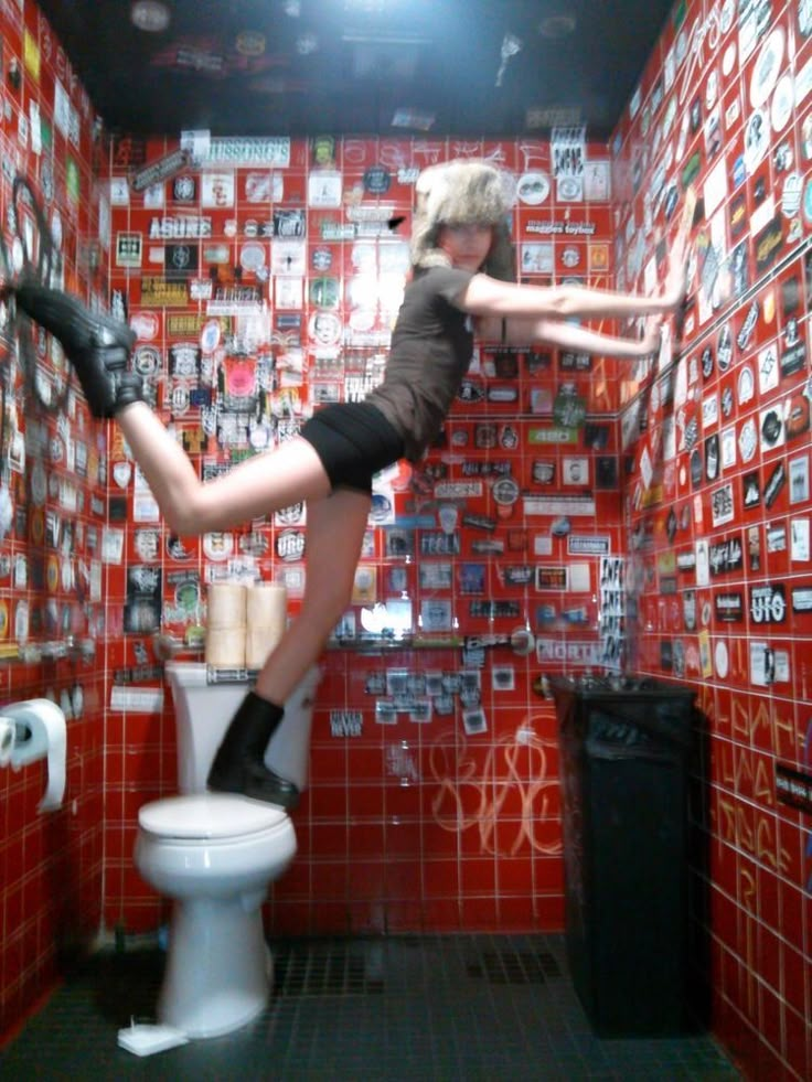 a woman standing on top of a toilet in a room filled with red and white tiles