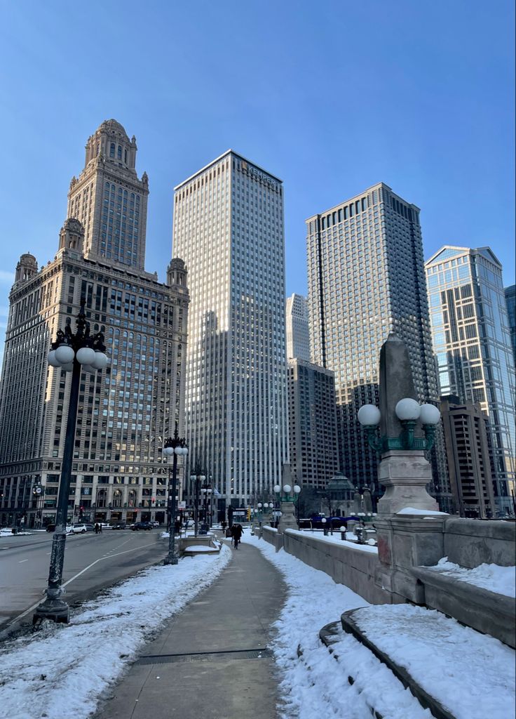 the city is covered in snow and has tall buildings on both sides, along with street lights